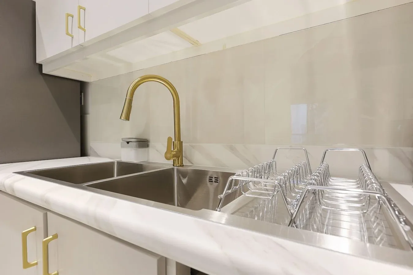A kitchen sink with a gold faucet and a dish rack on the counter.