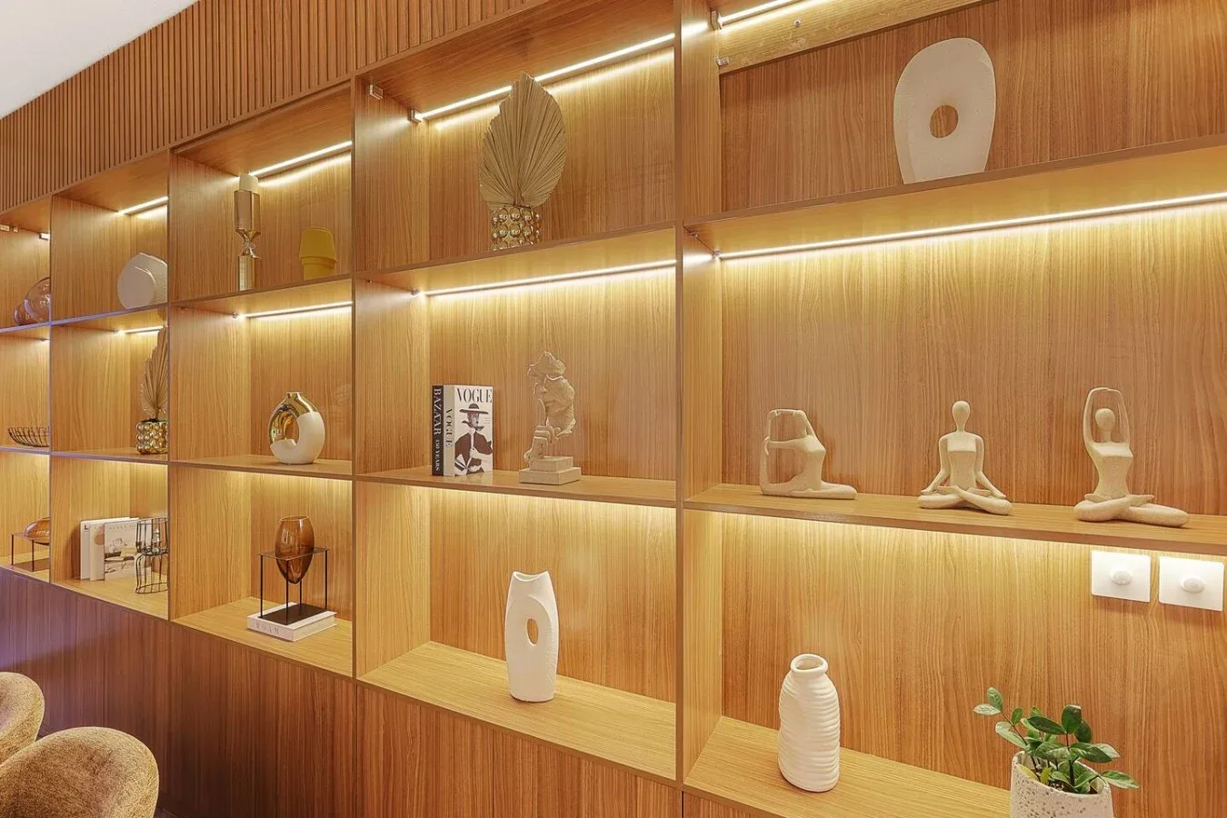 A warmly lit wooden display wall holds decorative objects and small sculptures.