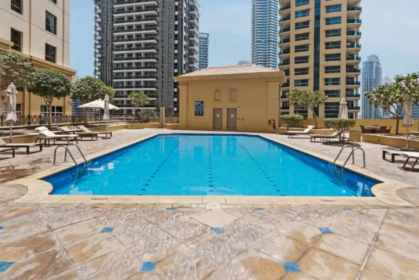 An outdoor swimming pool is surrounded by lounge seating and tall residential buildings.
