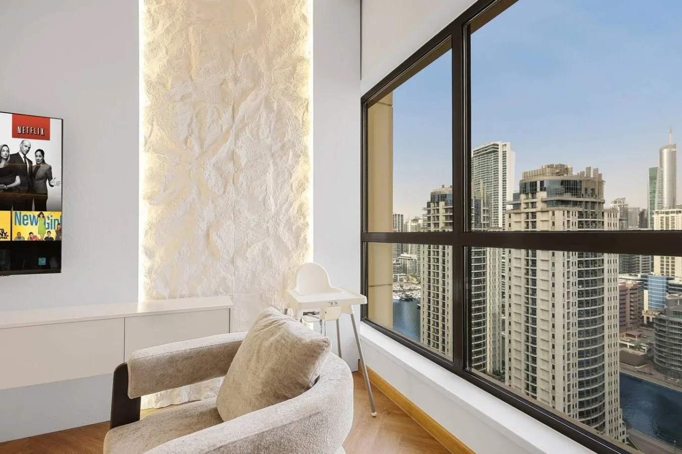 A bright living area with seating beside large windows overlooking city buildings.