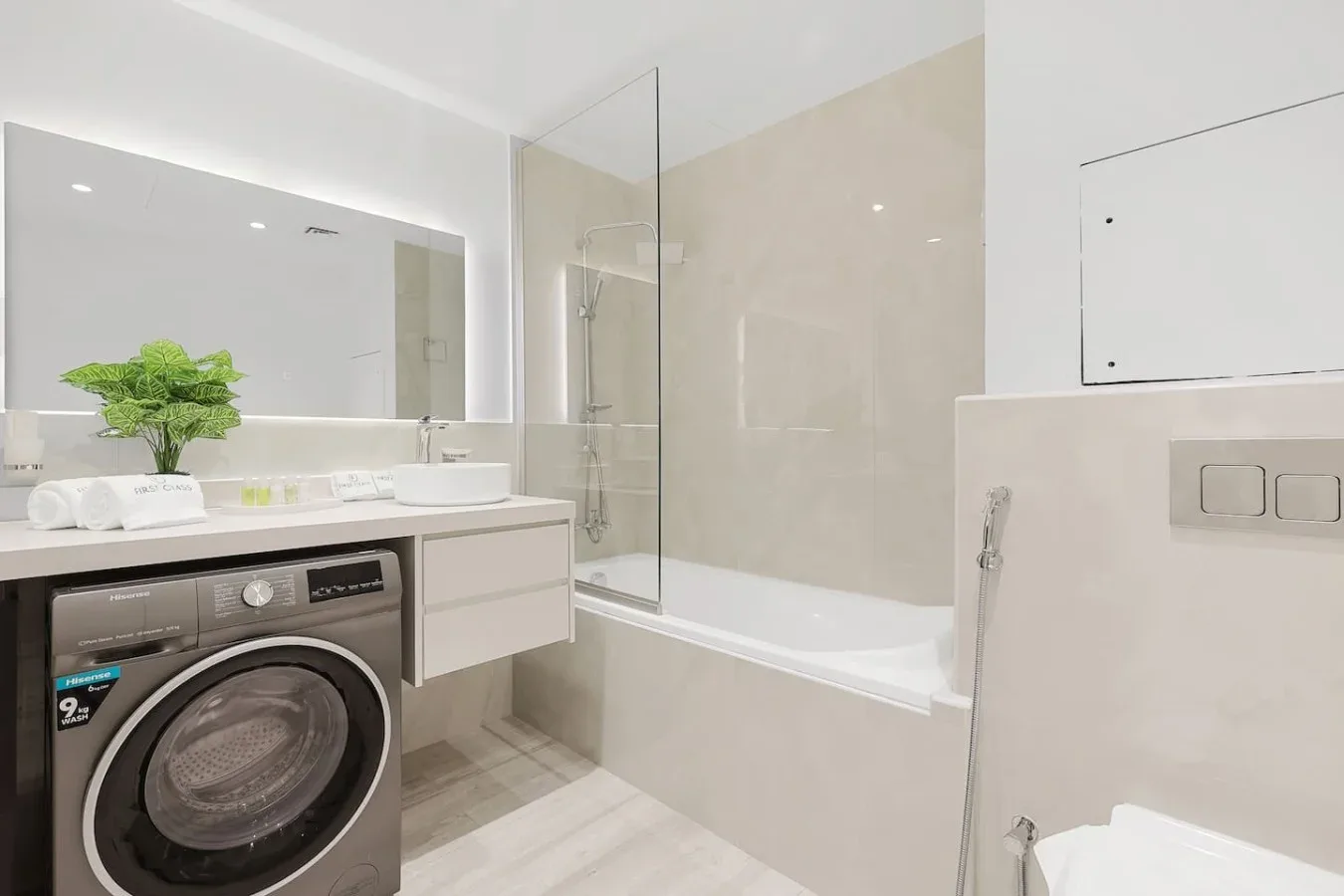 A bright bathroom with a bathtub, glass shower screen, and washing machine.