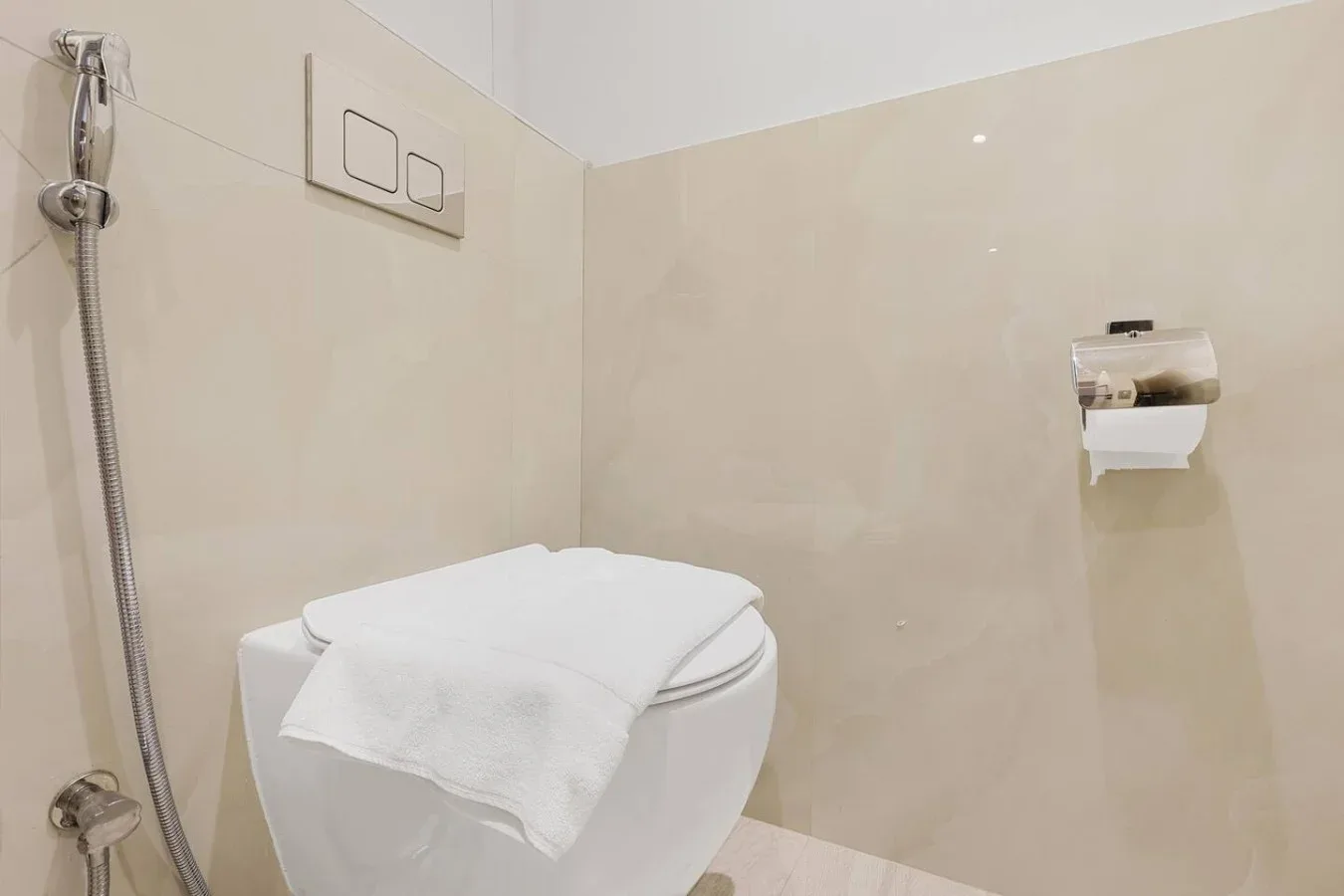 A bathroom with a wall-mounted toilet and a handheld shower hose.