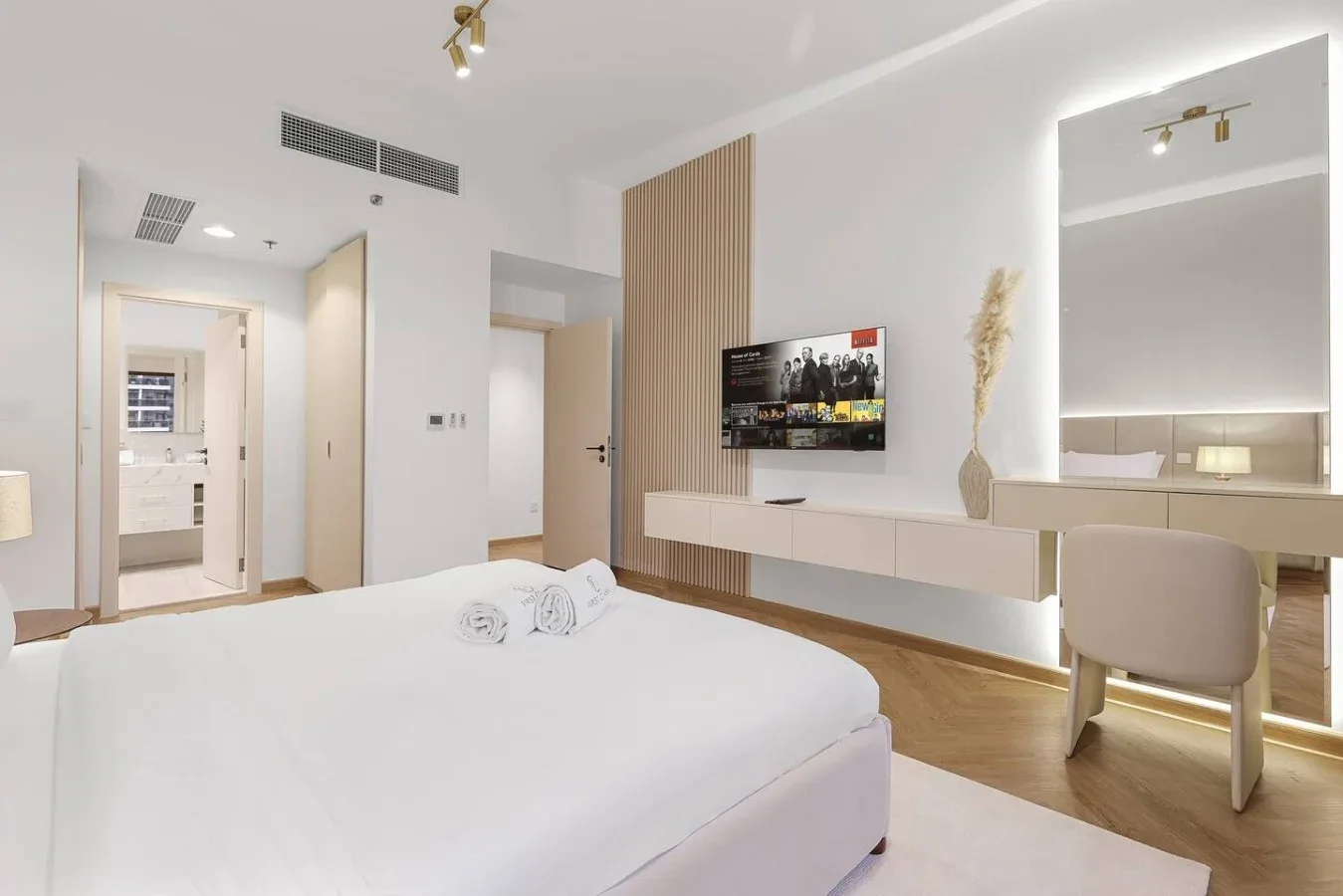 A bright bedroom with a bed, wall-mounted television, and desk.