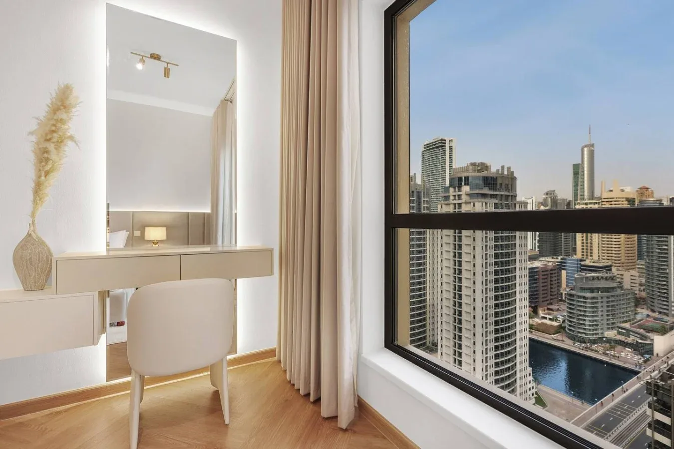 A bright room with a vanity and chair beside a large window overlooking city buildings.