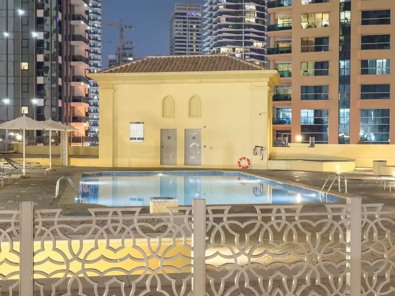 An outdoor swimming pool sits beside a small building, surrounded by high-rise buildings.