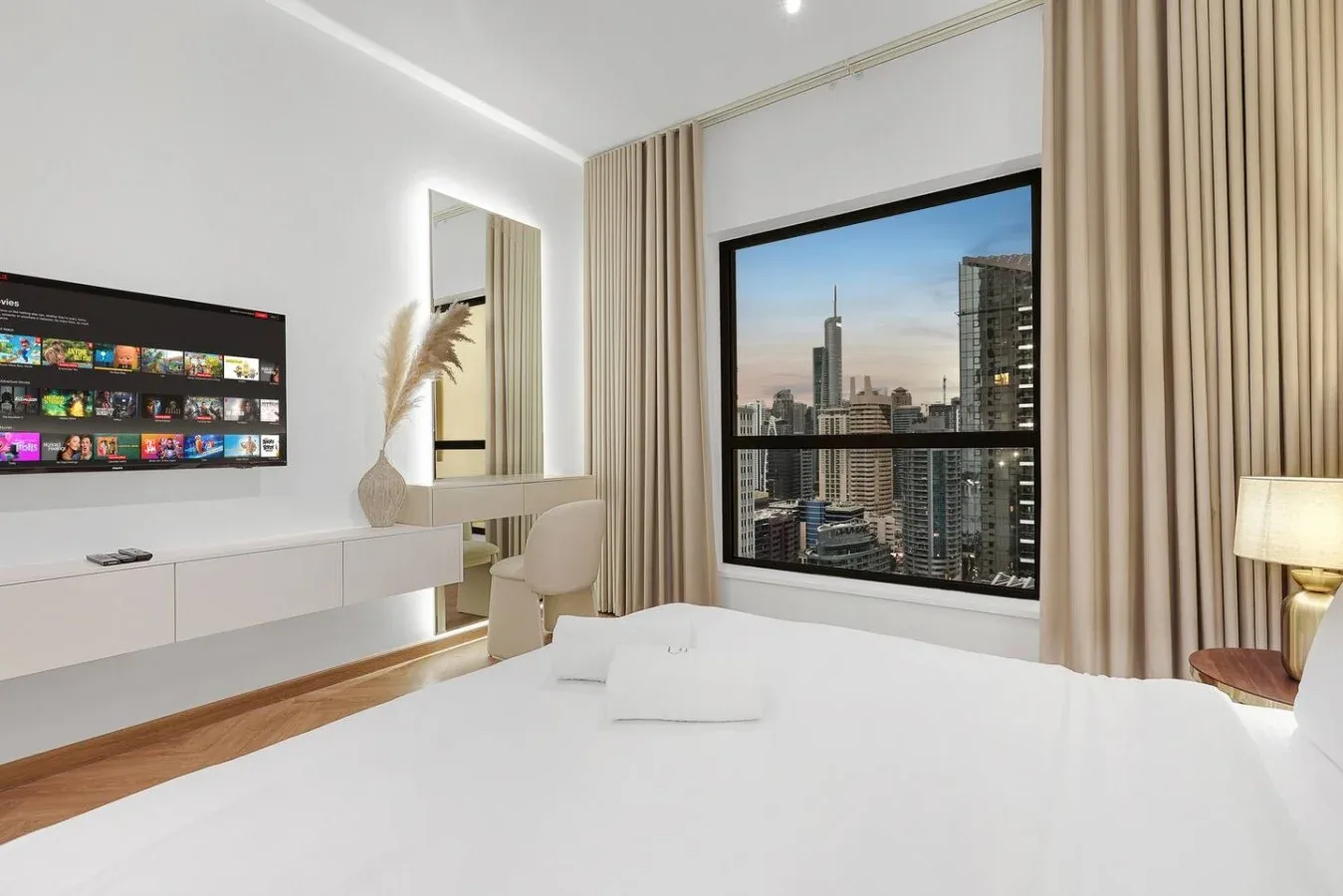 A bright bedroom with a large window overlooking a city skyline.