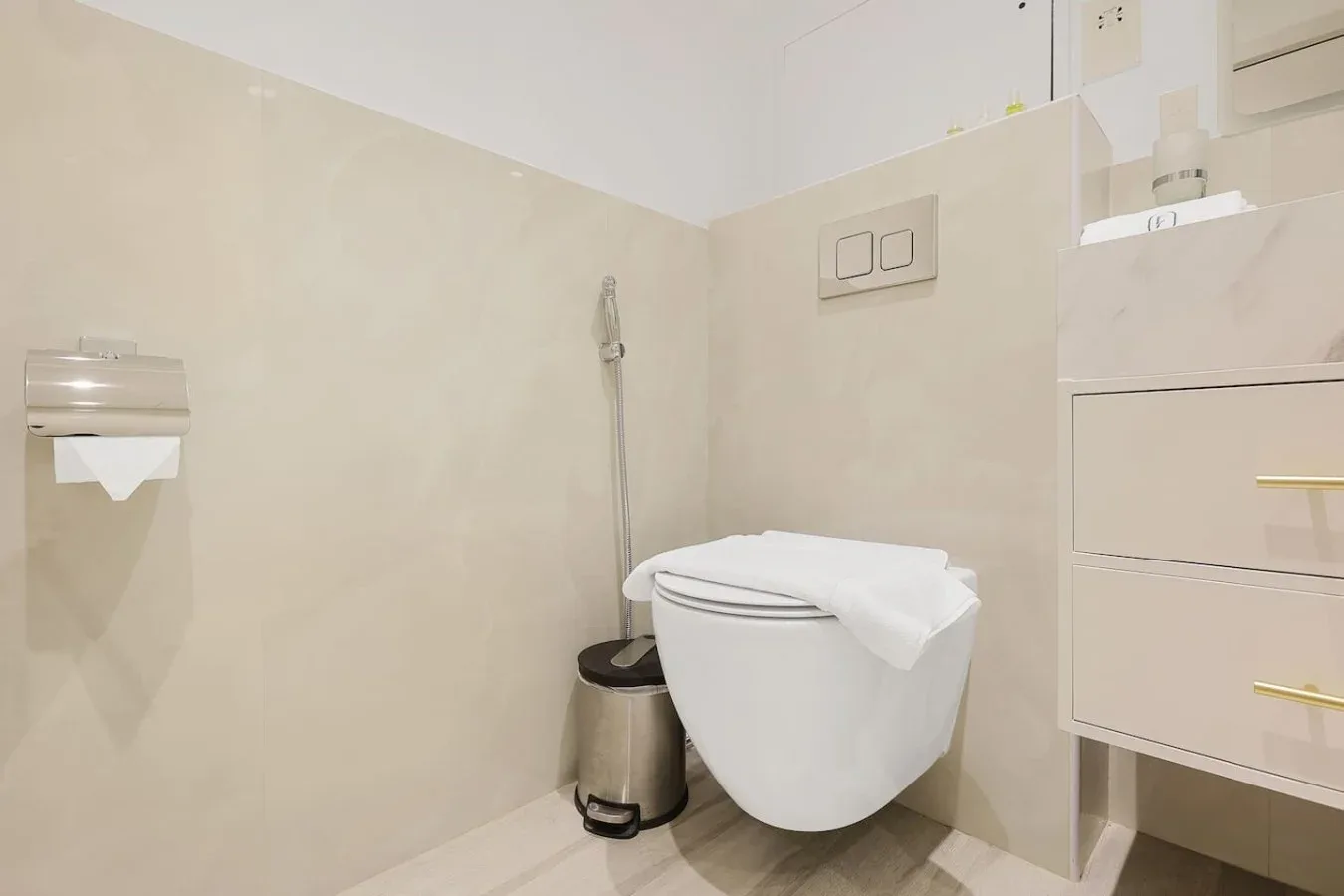 A bathroom with a wall-mounted toilet, handheld sprayer, and vanity.