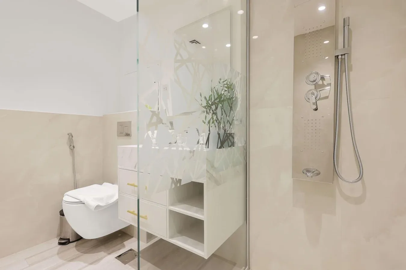 A bright bathroom with a glass shower and a wall-mounted toilet.