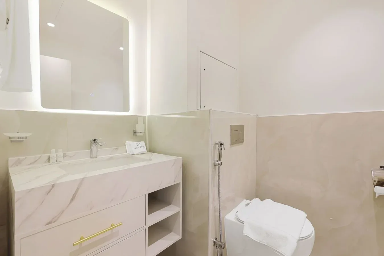 A bright bathroom with a wide vanity, illuminated mirror, and toilet.