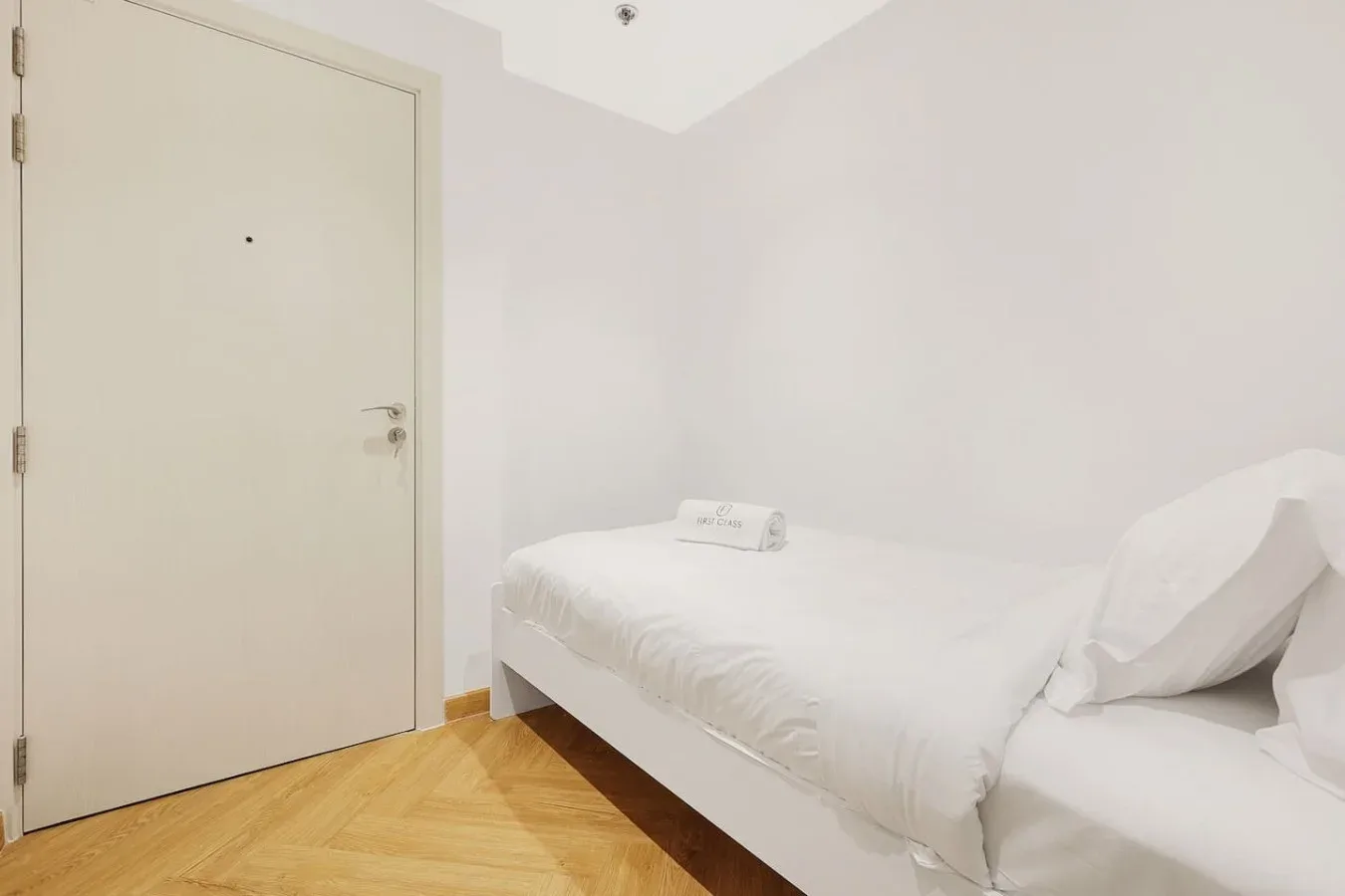 A bright bedroom with a neatly made bed beside a closed door.