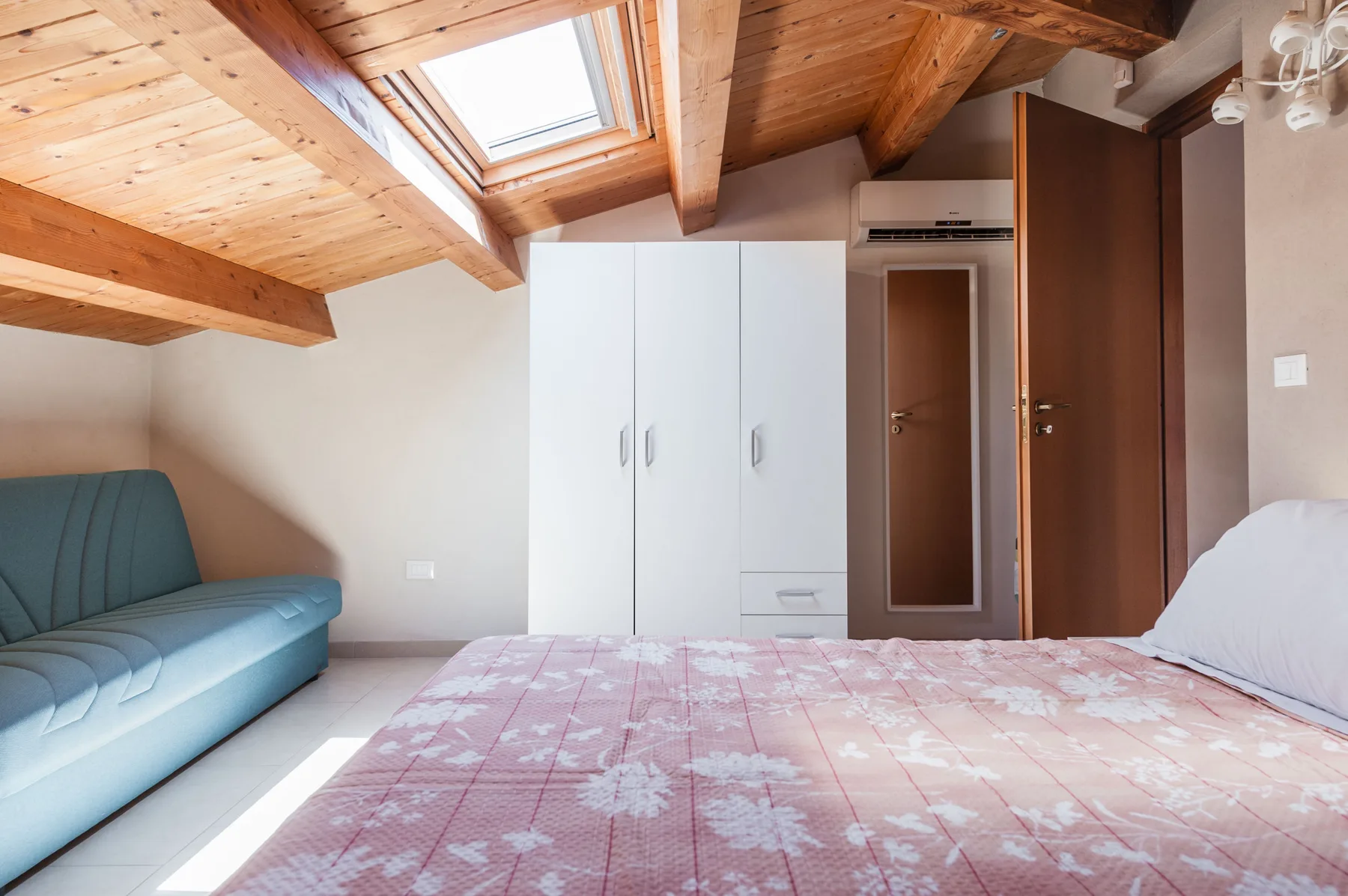 Un dormitorio con una cama, una zona de asientos azul y una claraboya.