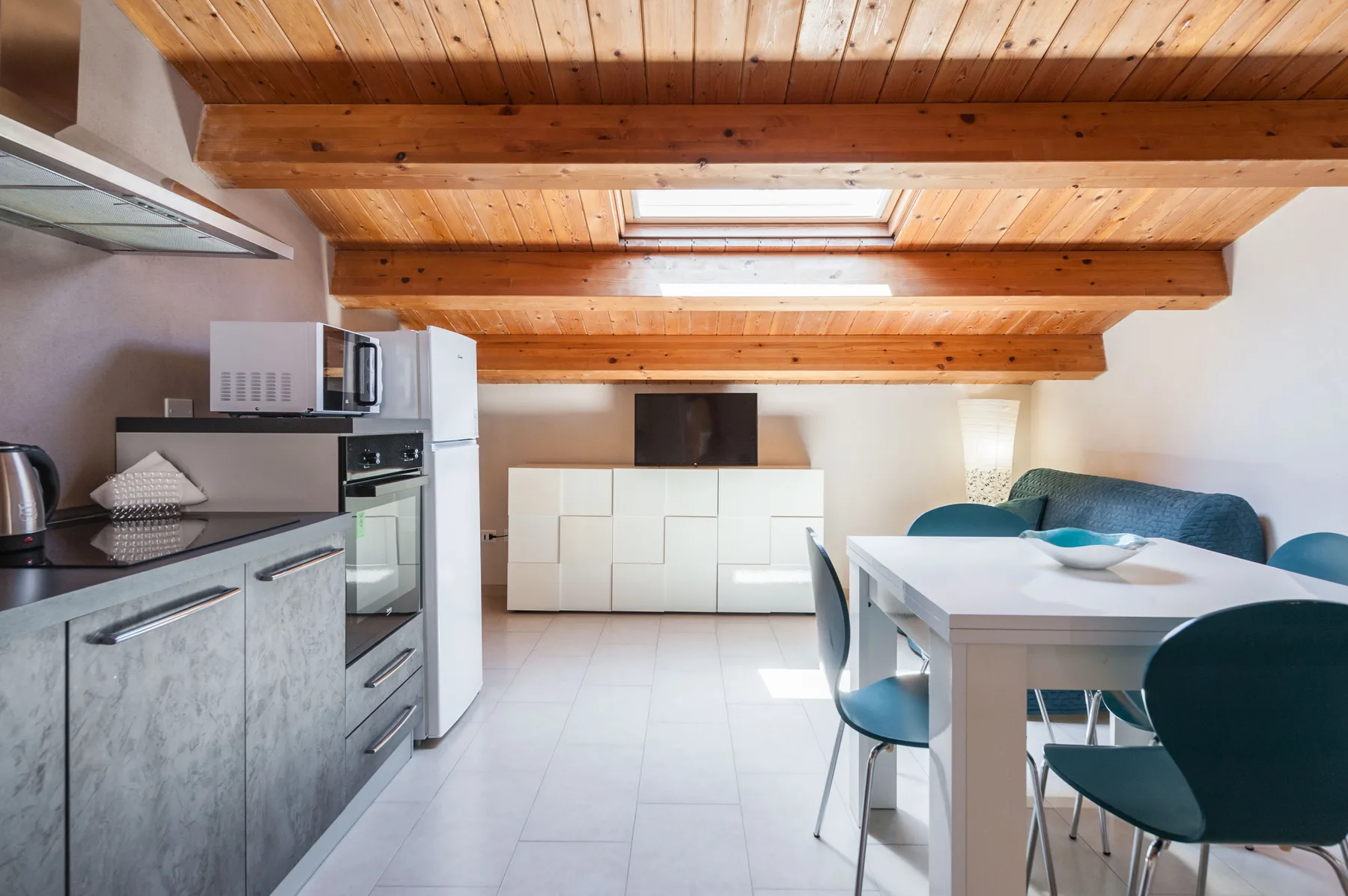 Una cocina y comedor luminosos con vigas de madera en el techo y una mesa blanca.