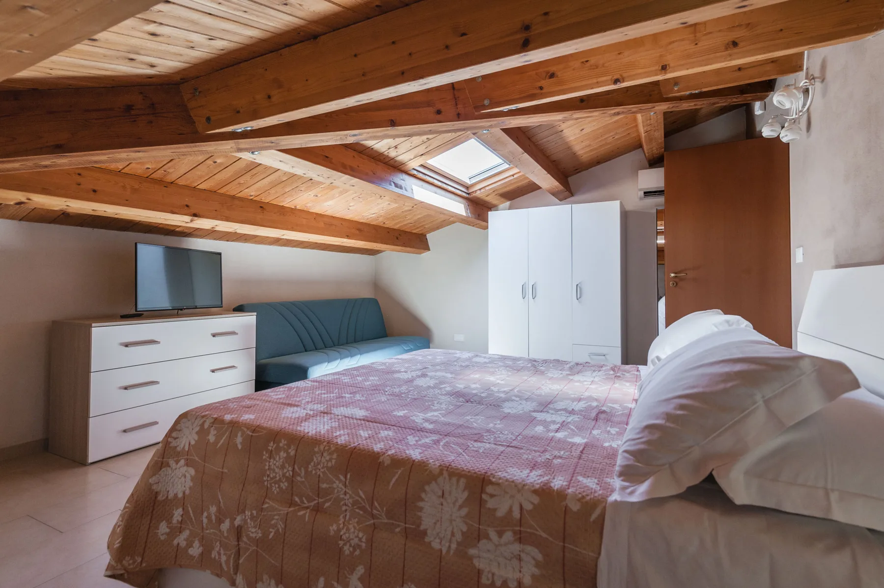 Un dormitorio con cama, armario y claraboya bajo un techo de madera inclinado.