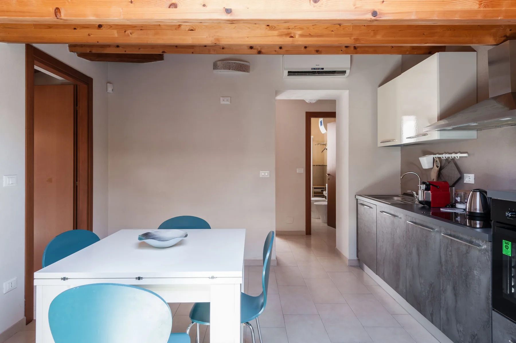Comedor y cocina con una mesa blanca y asientos turquesa.