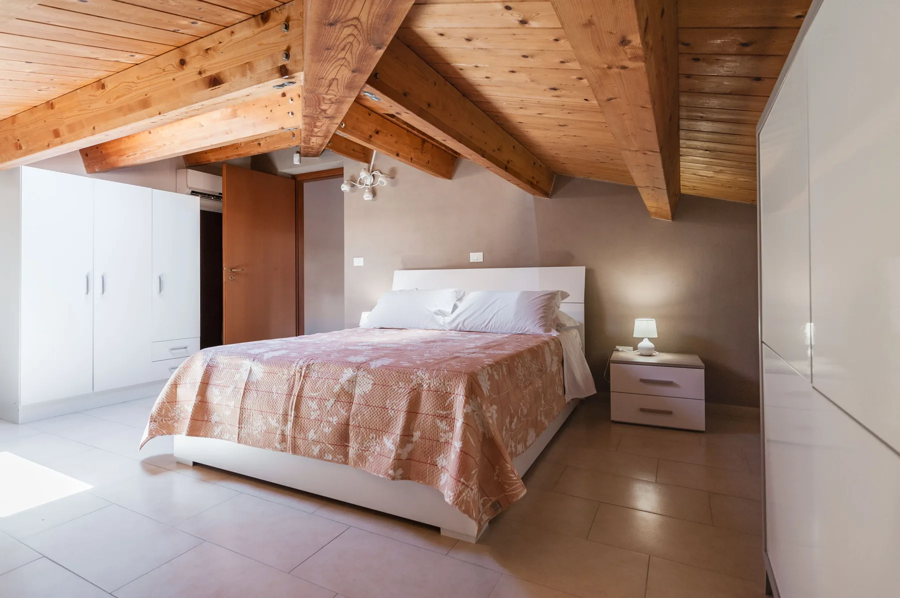 Un dormitorio con una cama bajo un techo inclinado de madera y armarios.