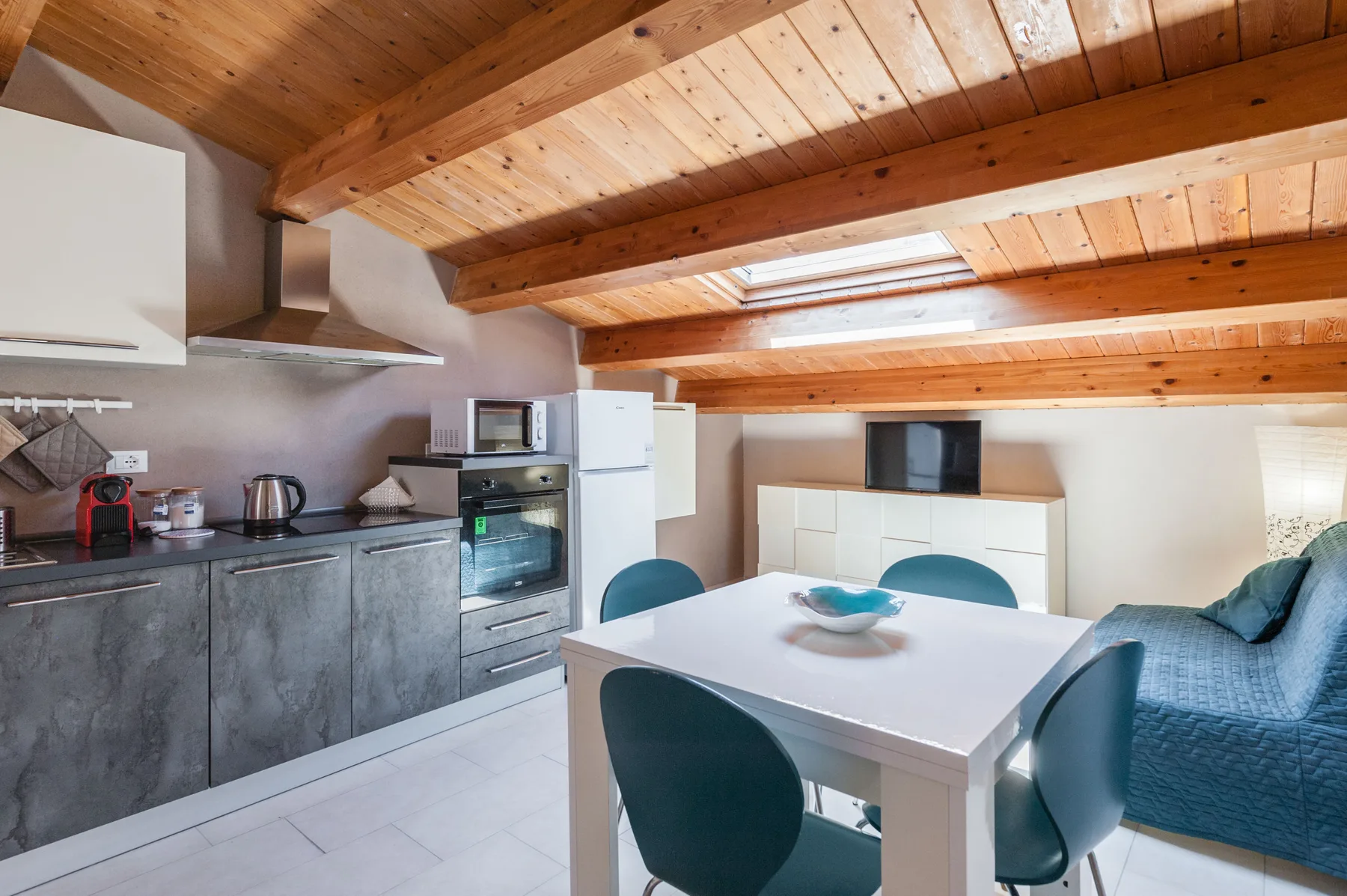 Una cocina y comedor con una mesa blanca bajo vigas de madera expuestas.