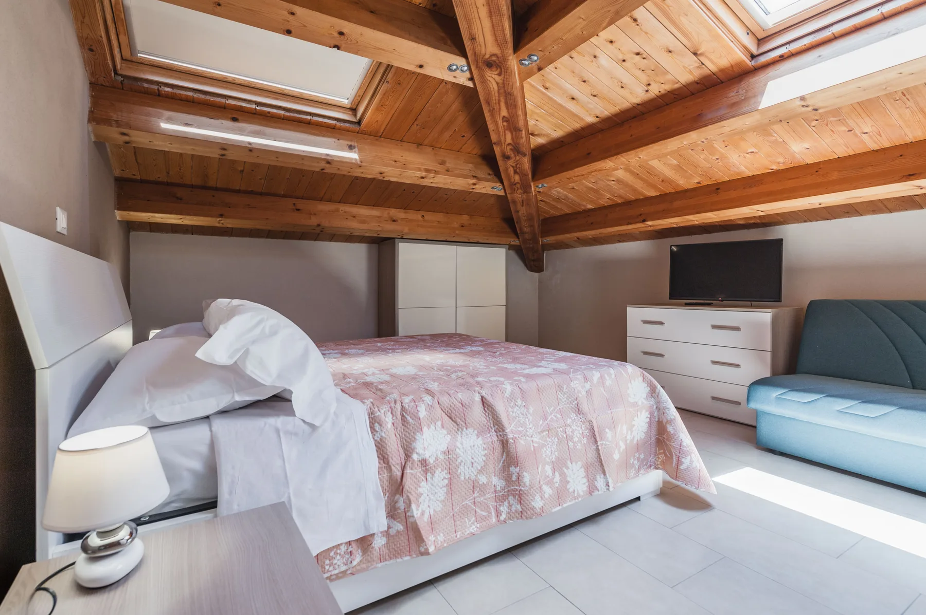 Un dormitorio con una cama bajo un techo inclinado de madera y tragaluces.