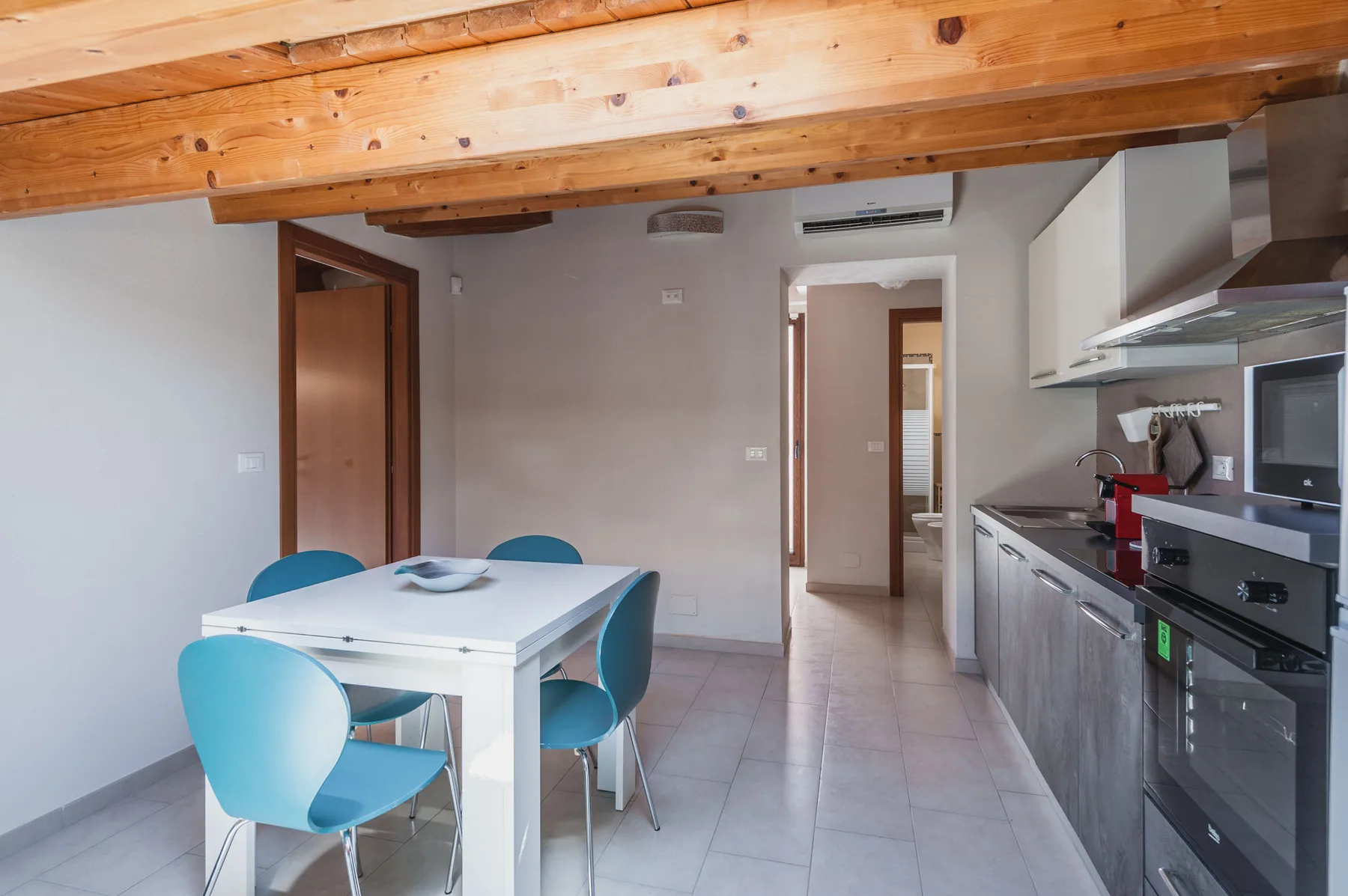 Una cocina y comedor con una mesa blanca, asientos azules y electrodomésticos integrados.