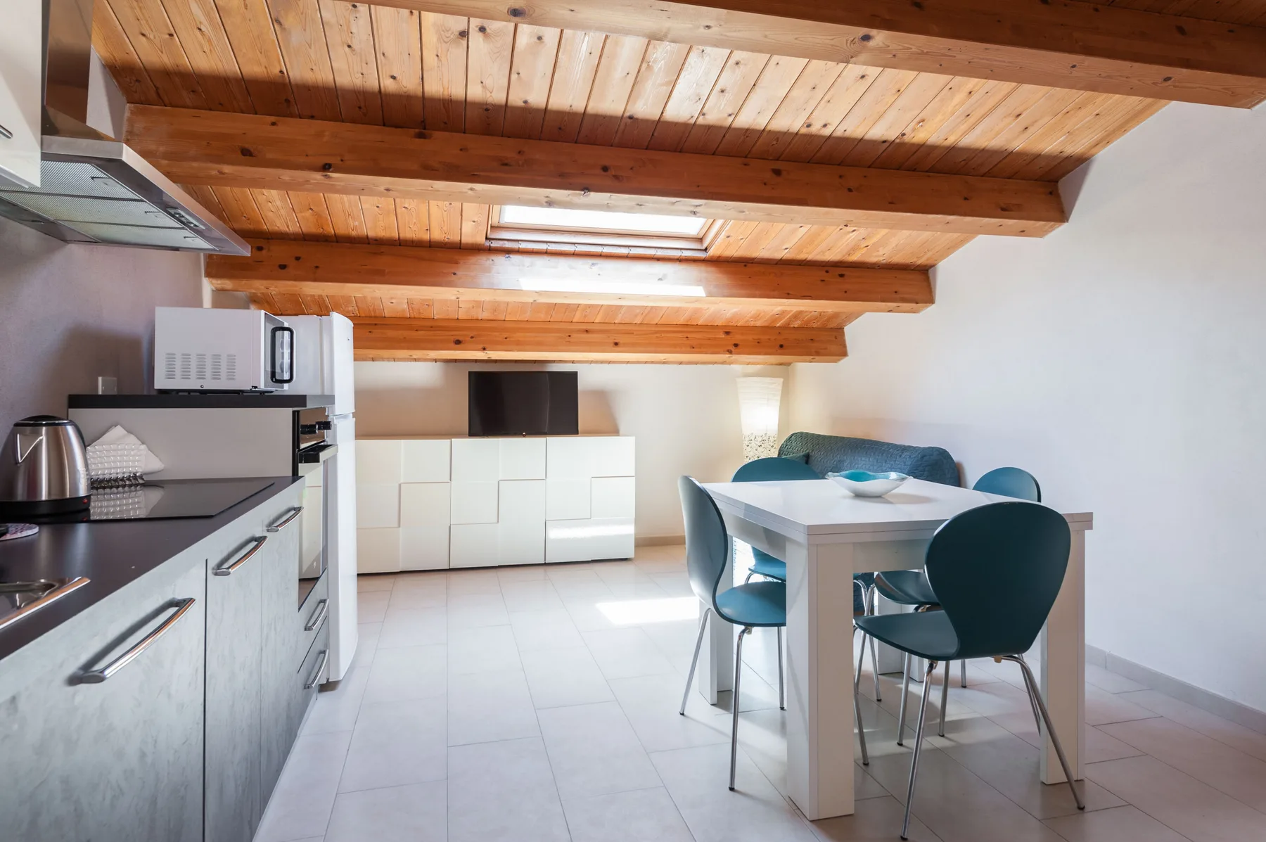 Una cocina y comedor con vigas de madera en el techo y una mesa blanca.