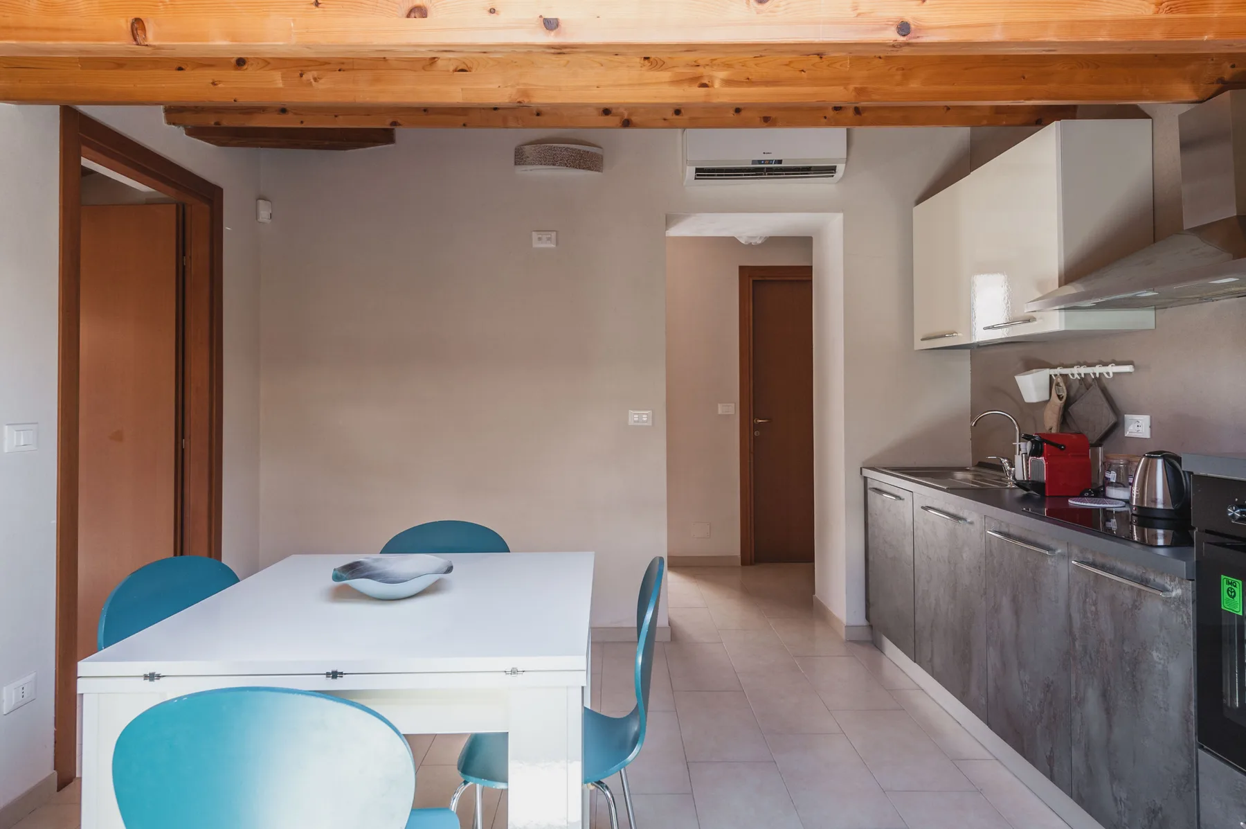 Comedor junto a una cocina compacta, con una mesa blanca y sillas.