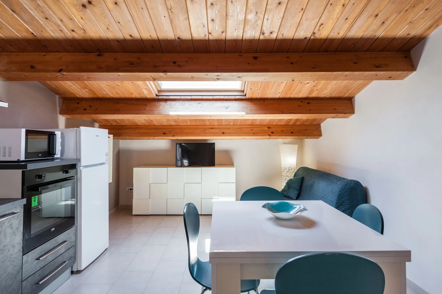 Una cocina compacta y zona de comedor con una mesa blanca bajo vigas de madera vistas.