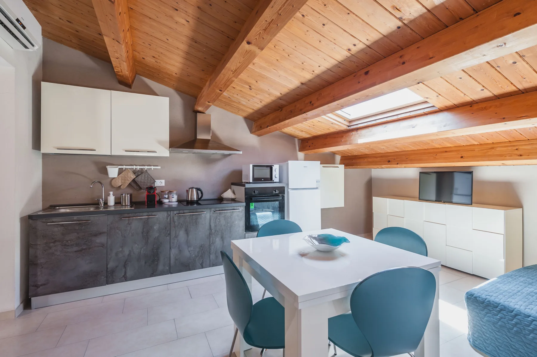 Cocina y comedor con una mesa bajo un techo revestido de madera.