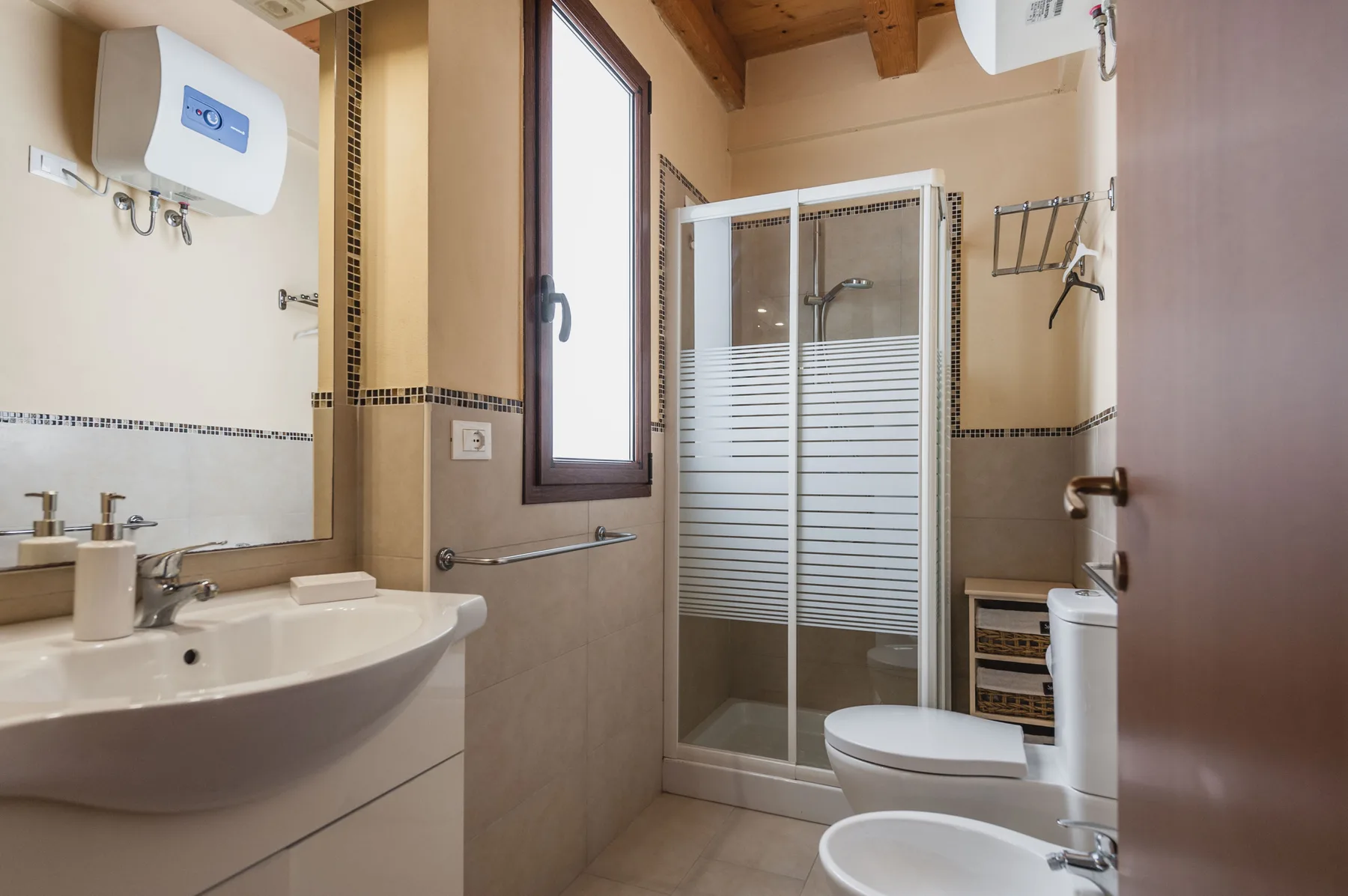 Un baño con lavabo, ducha e inodoro bajo vigas de madera a la vista.