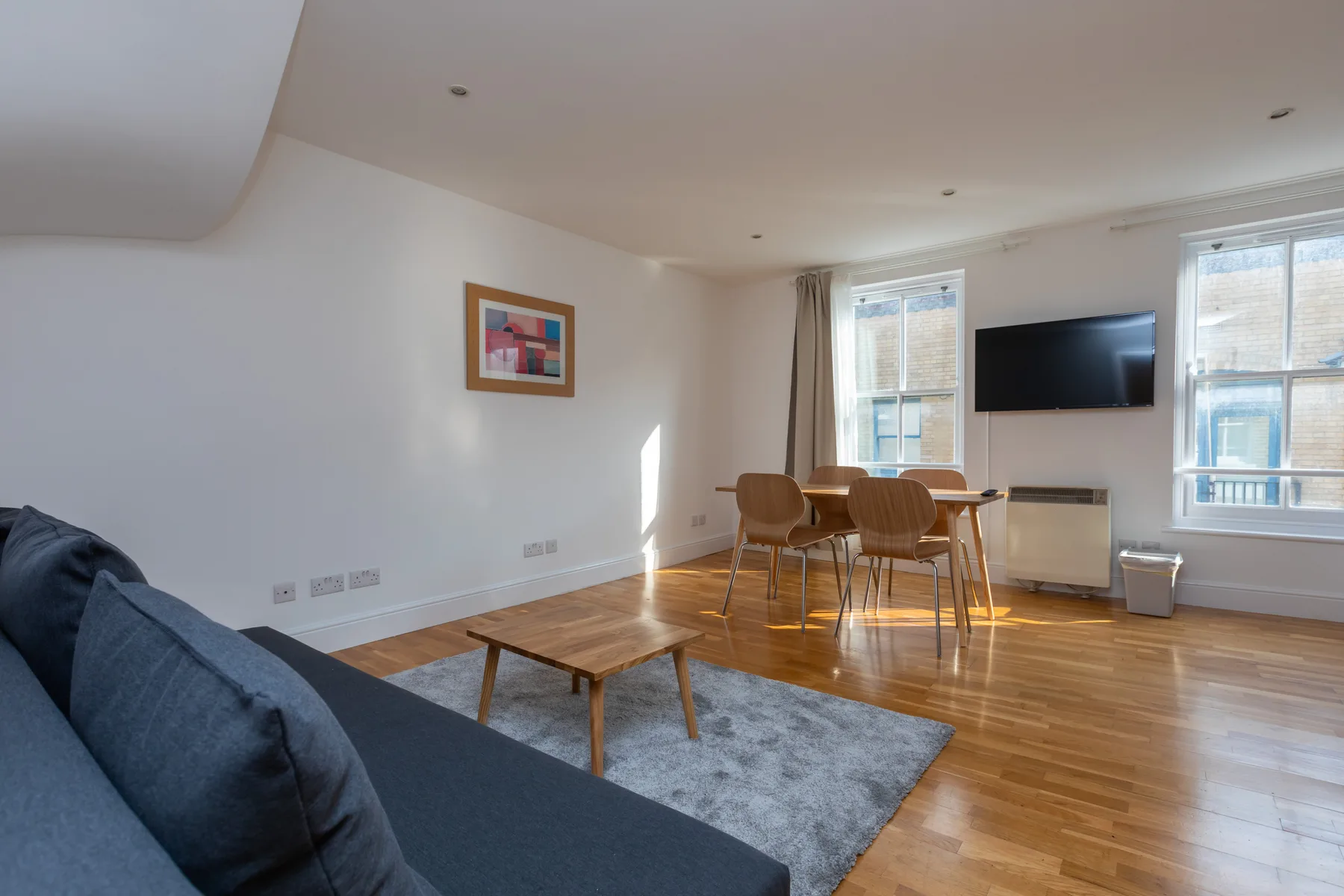 A bright living room has a dining table, wall-mounted television, and seating.