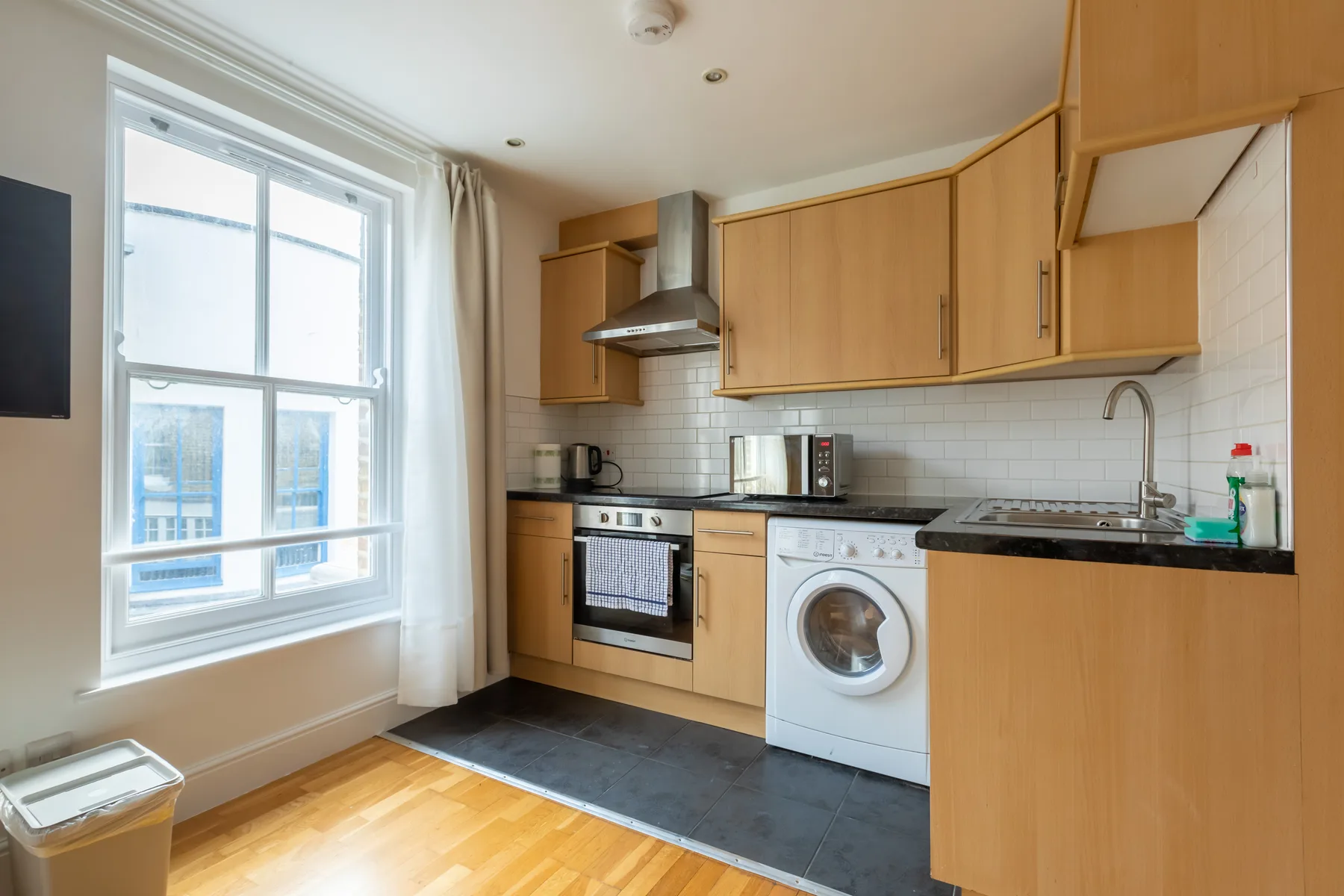 A compact kitchen with wood cabinets, a washing machine, and a large window.