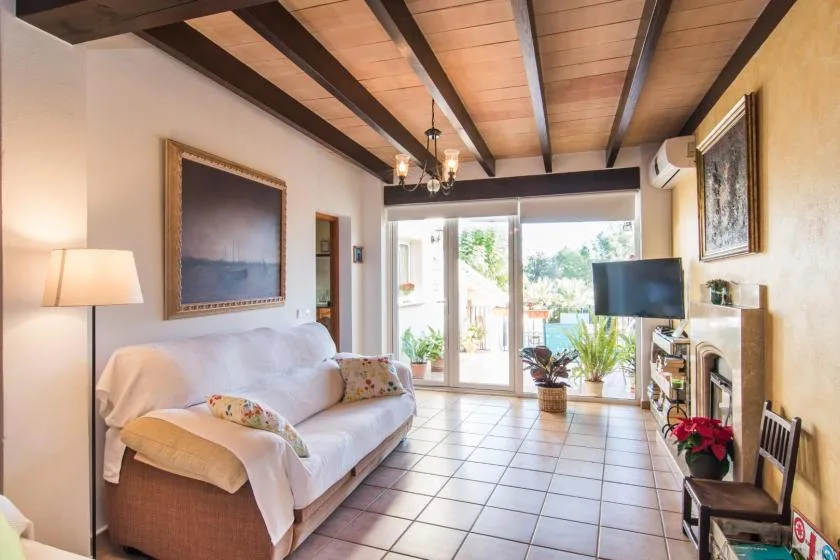 Una sala luminosa con asientos, un televisor y puertas de vidrio que dan a un jardín.