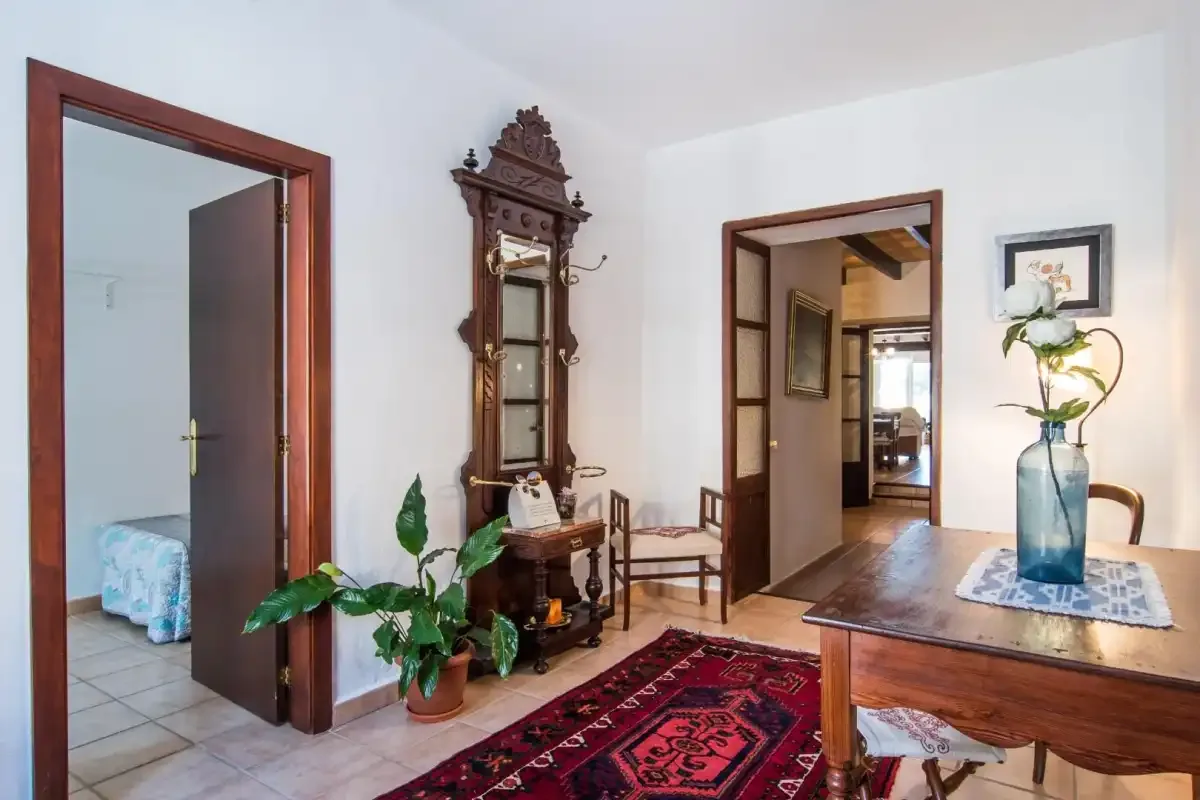 Un pasillo luminoso con puertas de madera, un reloj alto y una alfombra estampada.