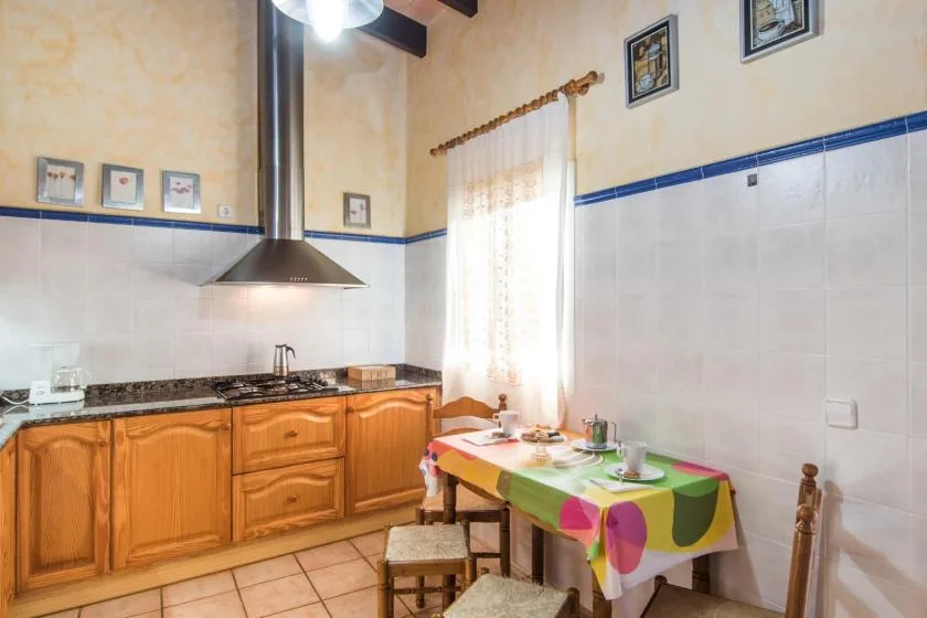 Una cocina con armarios de madera y una mesa pequeña junto a una ventana luminosa.