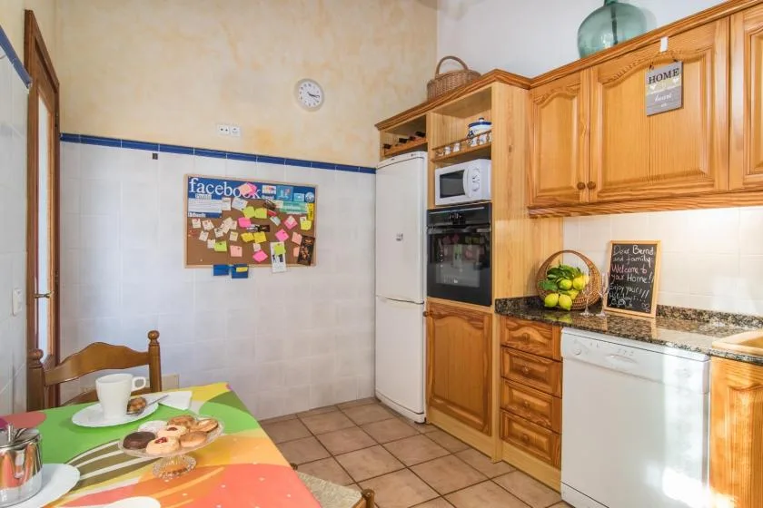 Una cocina con gabinetes de madera, un refrigerador y una mesa de comedor colorida.