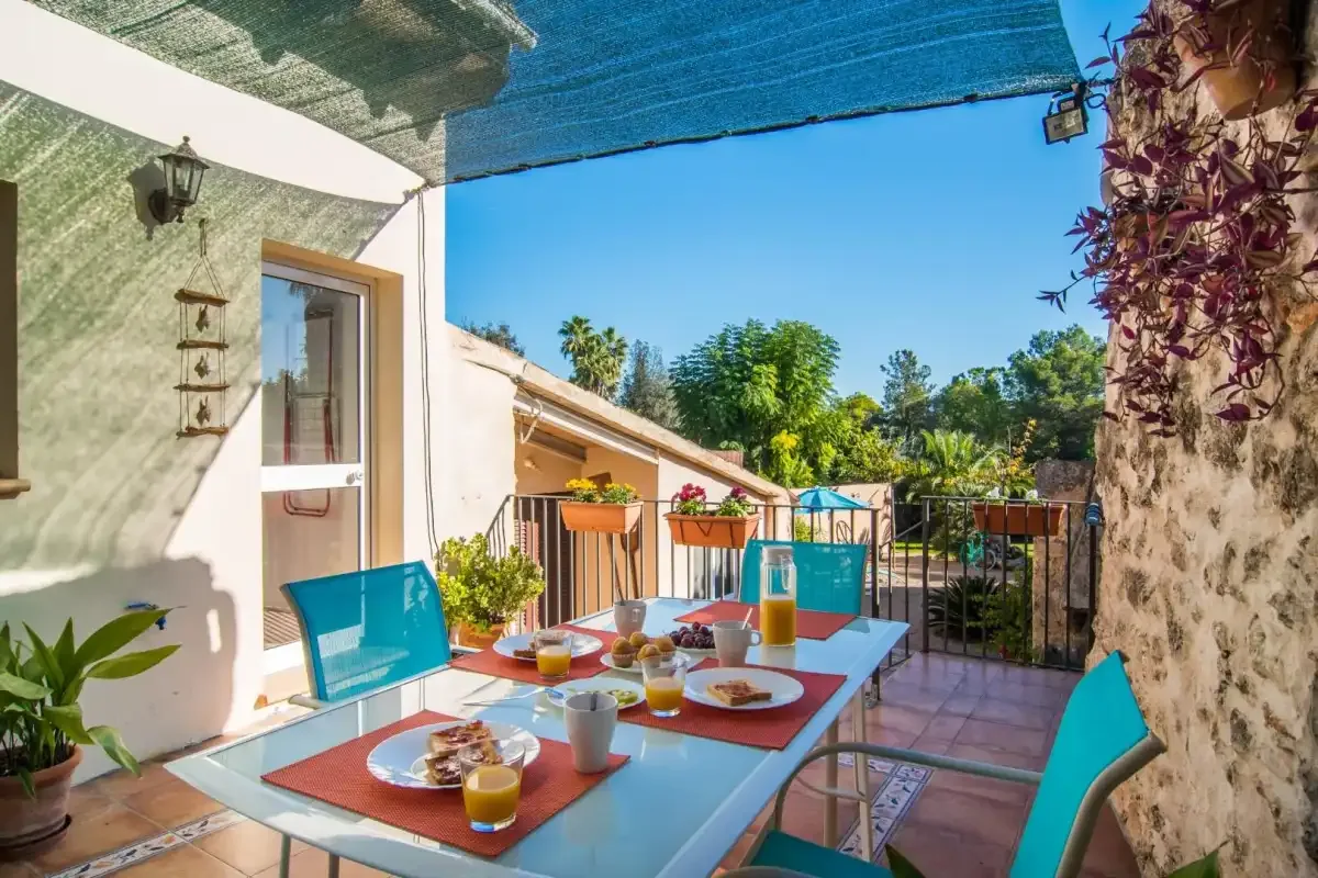 Un patio comedor al aire libre con una mesa puesta, asientos y un toldo azul.