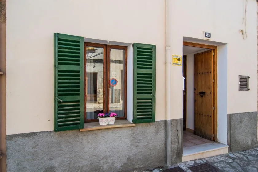 Una entrada de edificio con una puerta de madera junto a una ventana con contraventanas verdes.