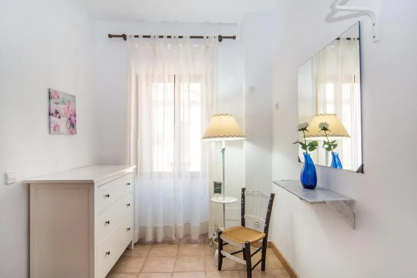 Un dormitorio luminoso con una cómoda, una silla y cortinas translúcidas en la ventana.