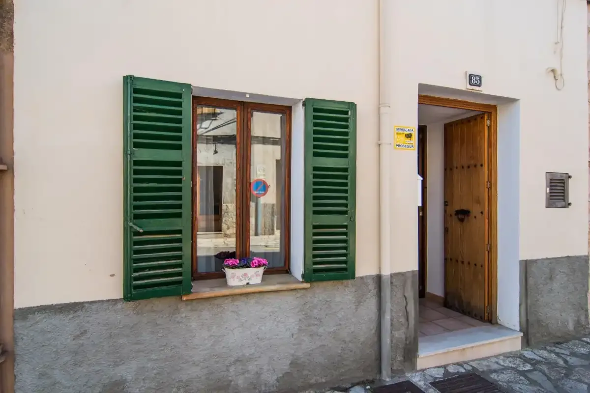 Una fachada con contraventanas verdes junto a una puerta de madera abierta.