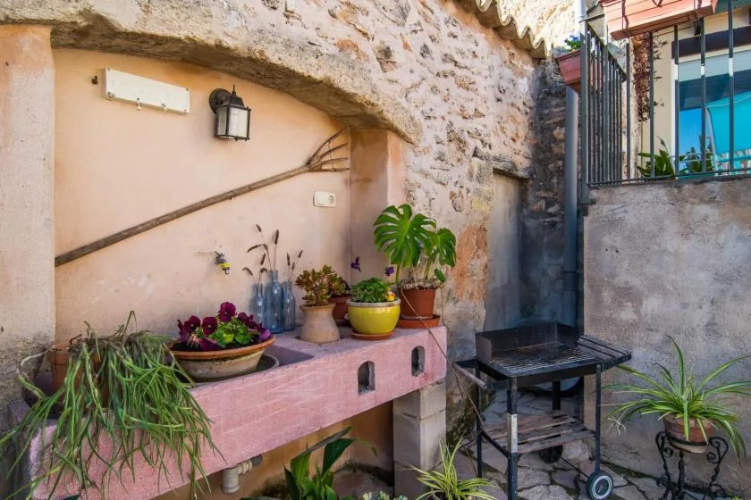 Un patio de piedra con un fregadero exterior rosa, plantas en macetas y una parrilla.