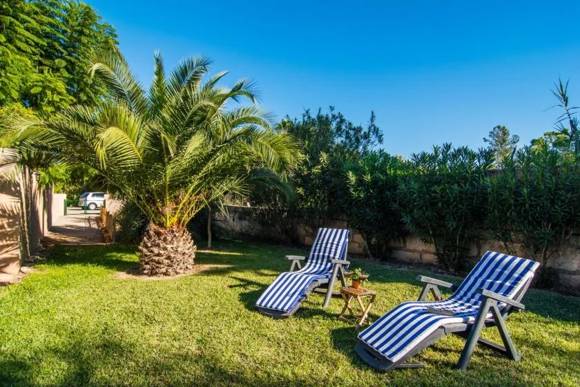 Un jardín con césped y tumbonas de rayas azules y blancas bajo palmeras.
