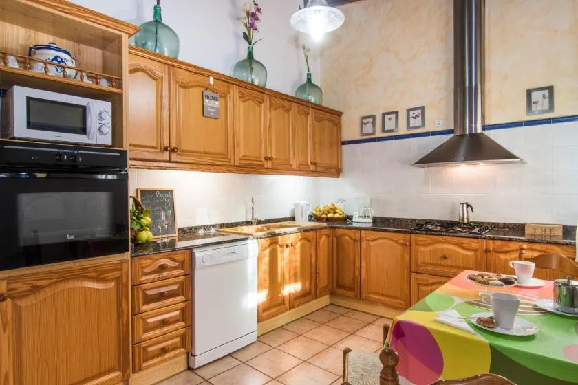 Una cocina de tonos cálidos con gabinetes de madera, electrodomésticos y una mesa colorida.