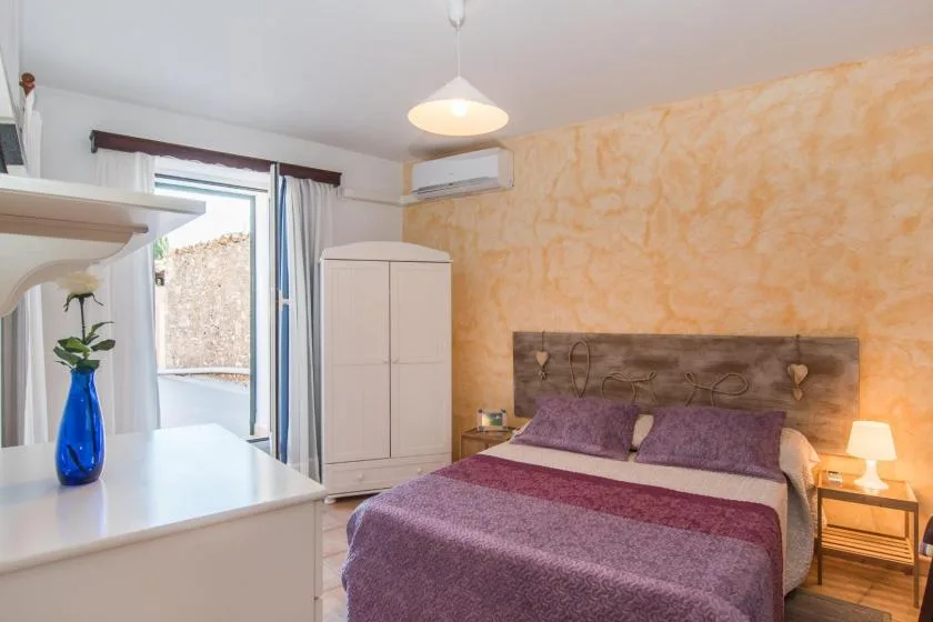Un dormitorio con cama doble, ropa de cama morada y un armario junto a la ventana.