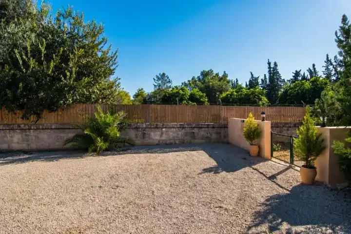 Un patio de grava con un muro bajo de piedra y árboles alrededor.