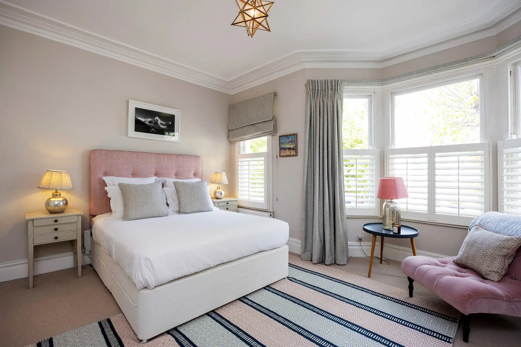 A bright bedroom with a bed, large windows, and a striped rug.