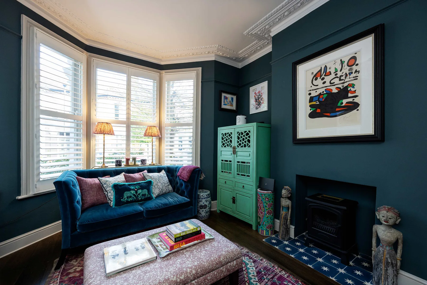 A living room with blue seating, tall windows, and a framed artwork.