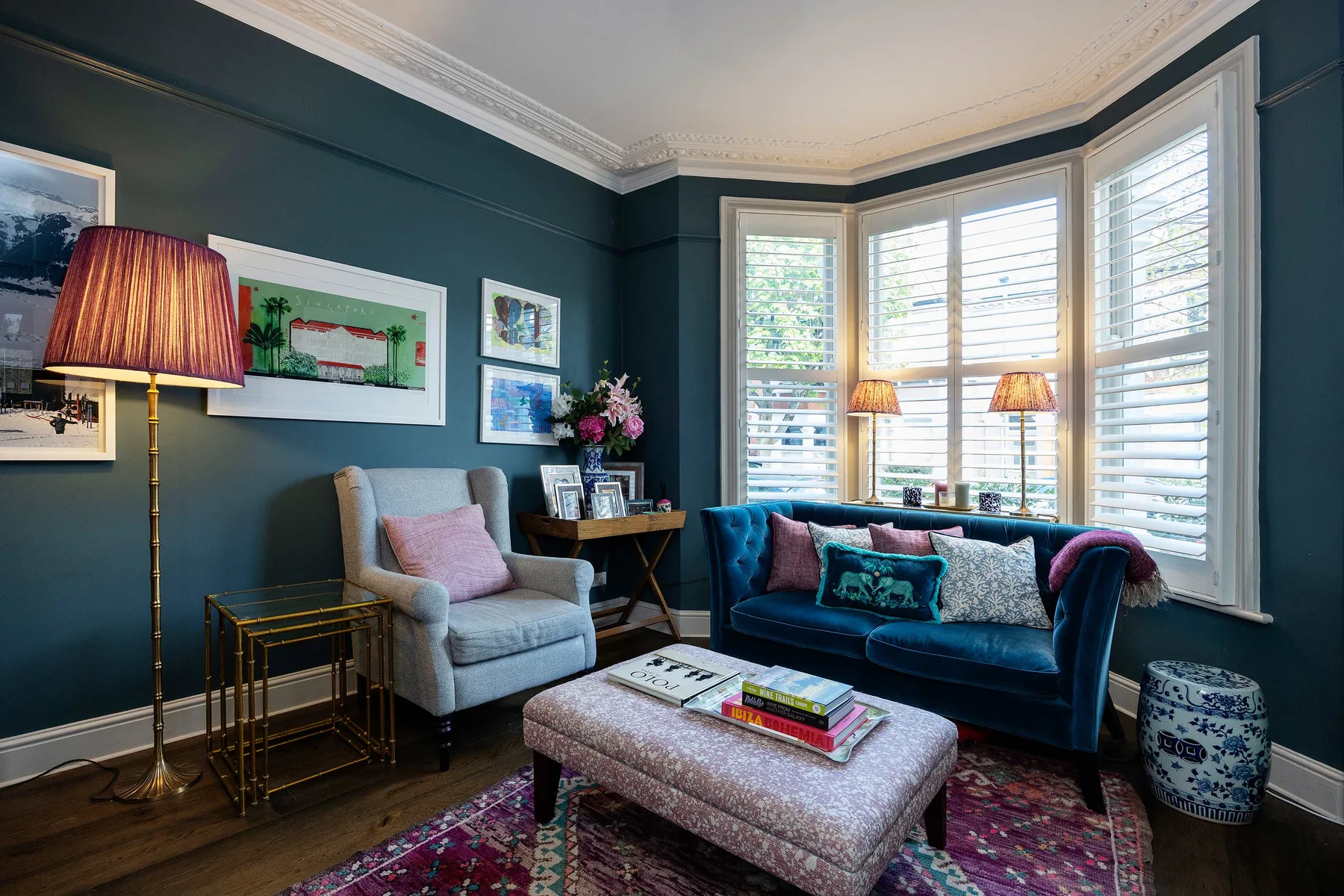 A living room with a blue sofa beside large windows with white blinds.