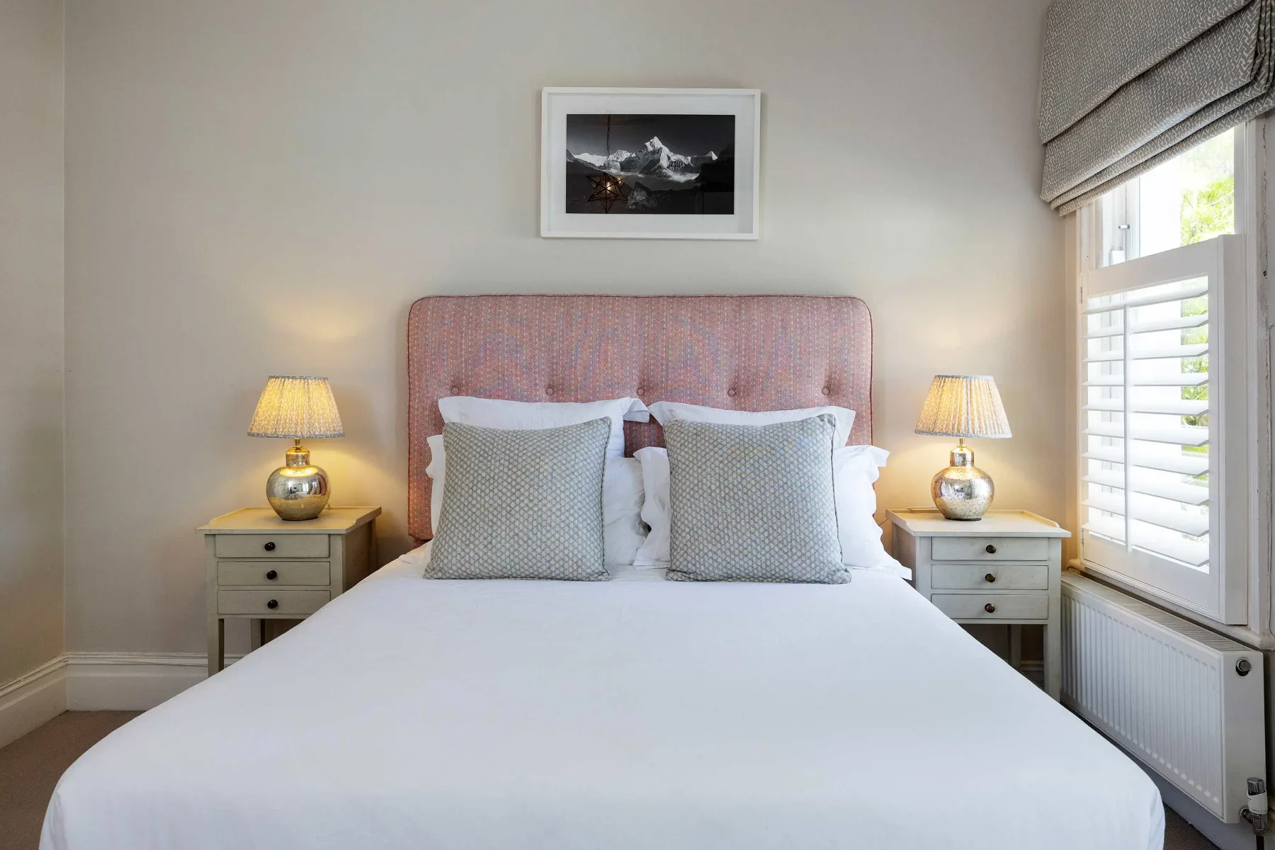 A bedroom with a neatly made bed between two bedside tables.