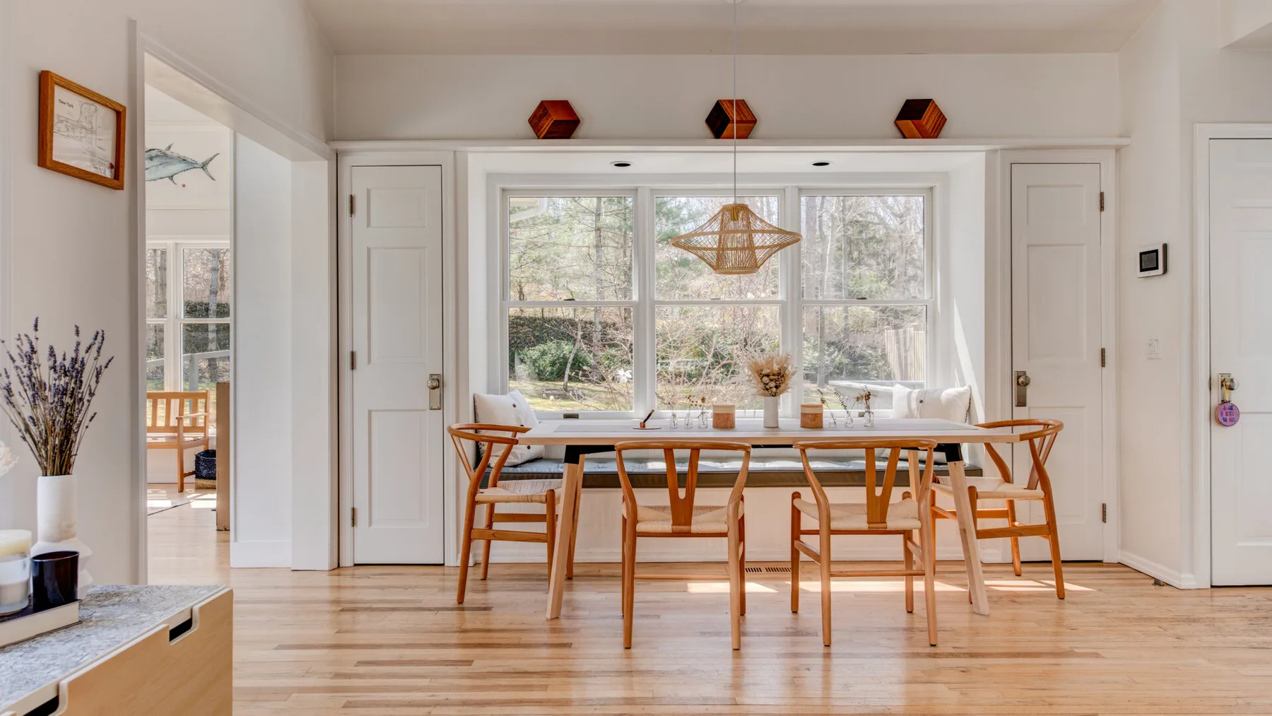 Un comedor luminoso tiene una mesa larga de madera y sillas junto a grandes ventanas.