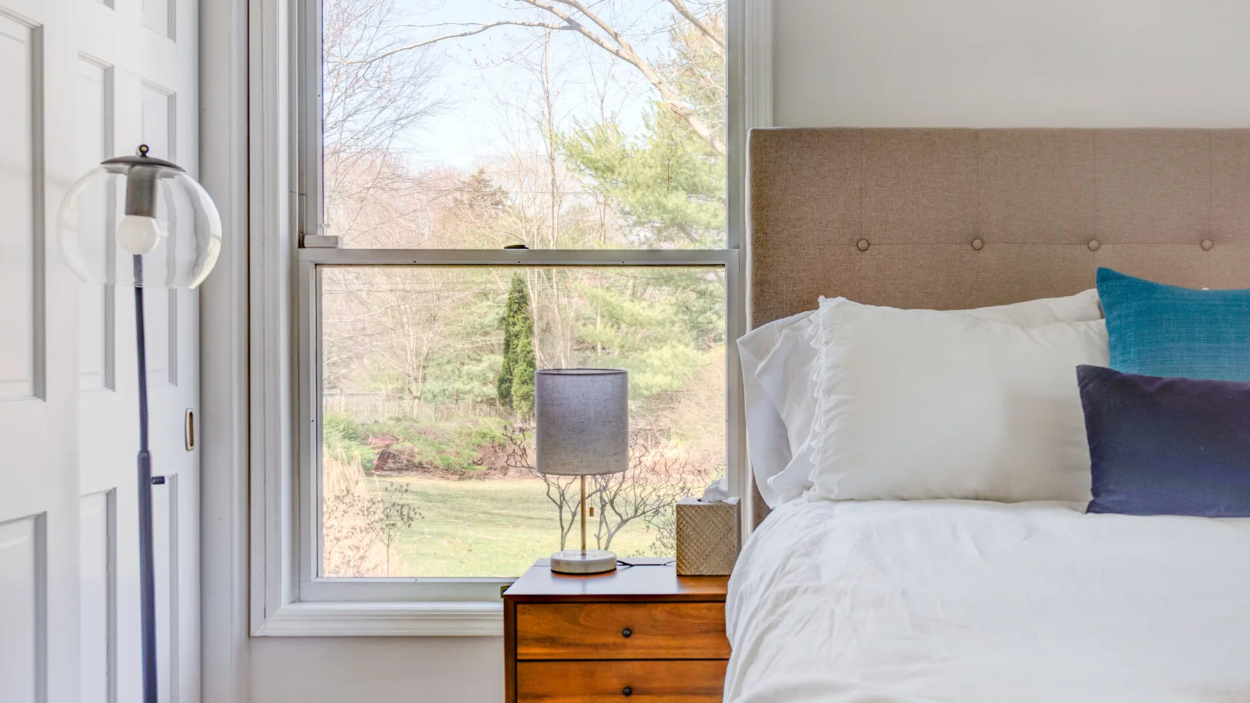 Un dormitorio con una cama bien tendida junto a una ventana grande.