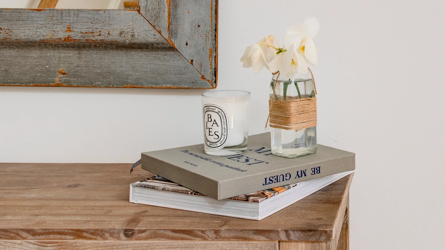 Una mesa de madera muestra libros, una taza estampada y un jarrón con flores blancas.