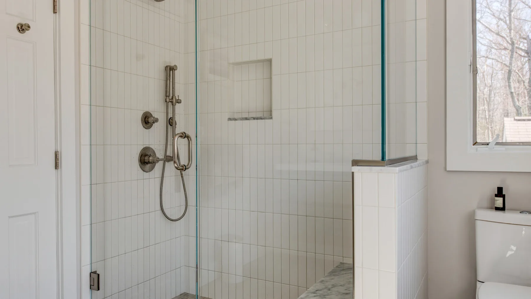 Un baño alicatado con ducha de vidrio y una ventana.